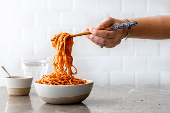 creamy gochujang noodles in bowl with chopsticks in hand lifting.