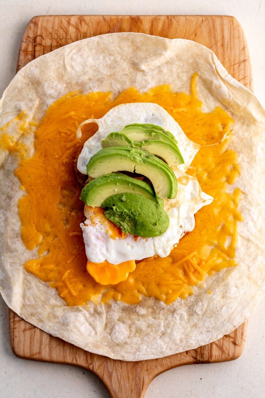 assembled piled breakfast burrito with melted cheese, hashbrowns, eggs and avocado.