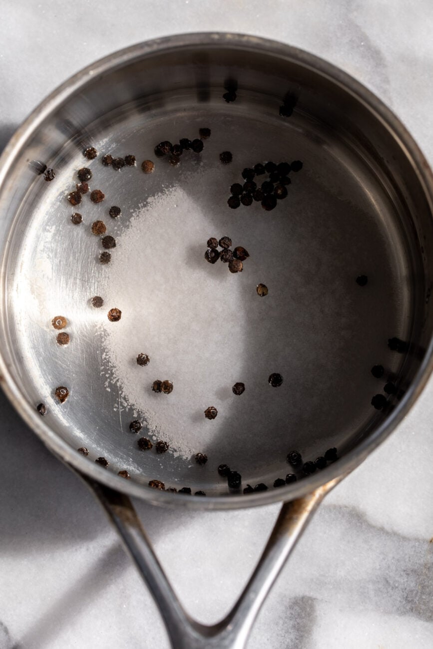Onion pickling brine in small saucepan with salt, sugar and black peppercorns.