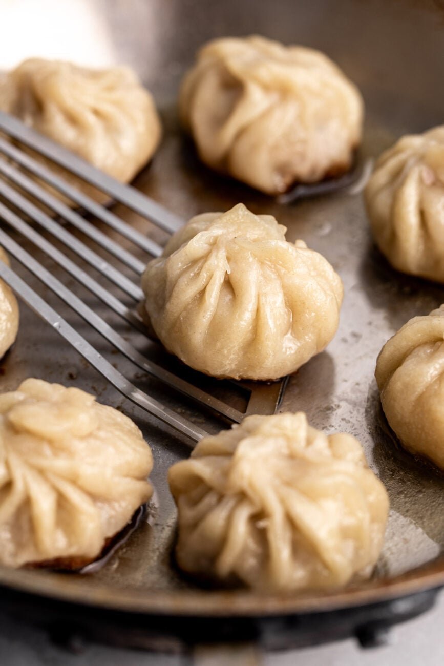 pan-fried dumplings in pan with fish spatula.