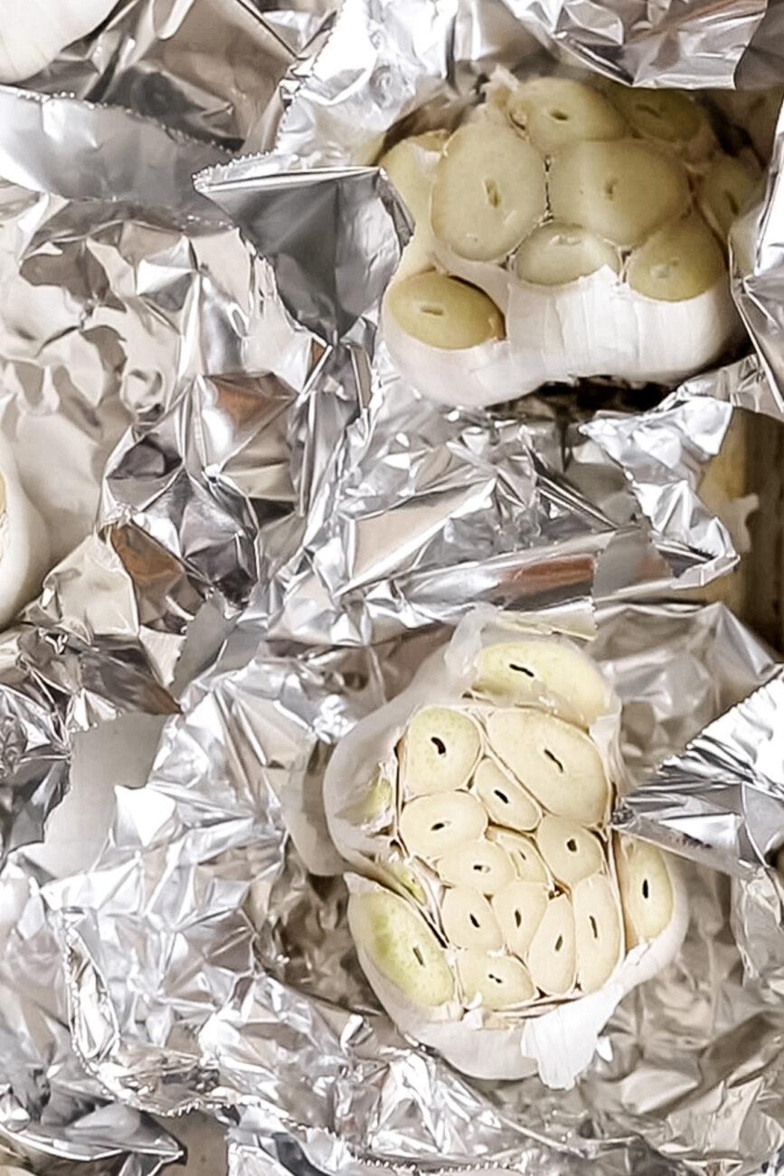 trimmed heads of garlic wrapped in aluminum foil.