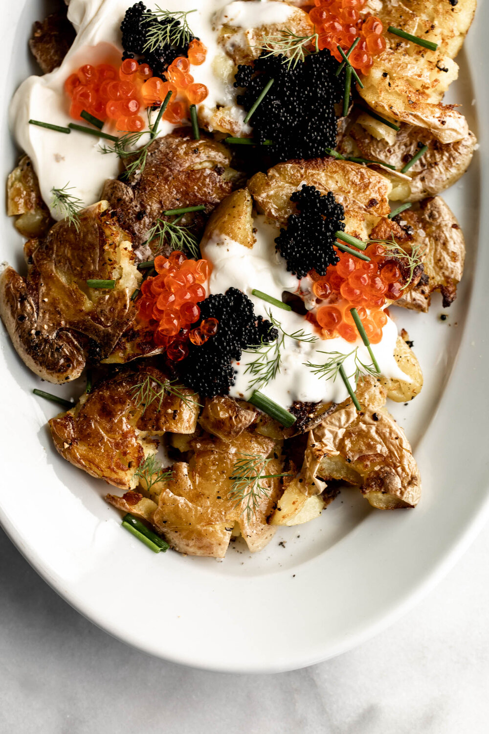 Crispy smashed fried potatoes are topped with creme fraiche, chives and caviar for a luxurious and indulgent holiday side.