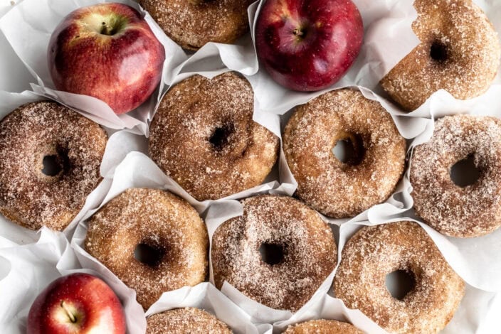 Apple Cider Donuts with red apples in the background in cinnamon sugar.
