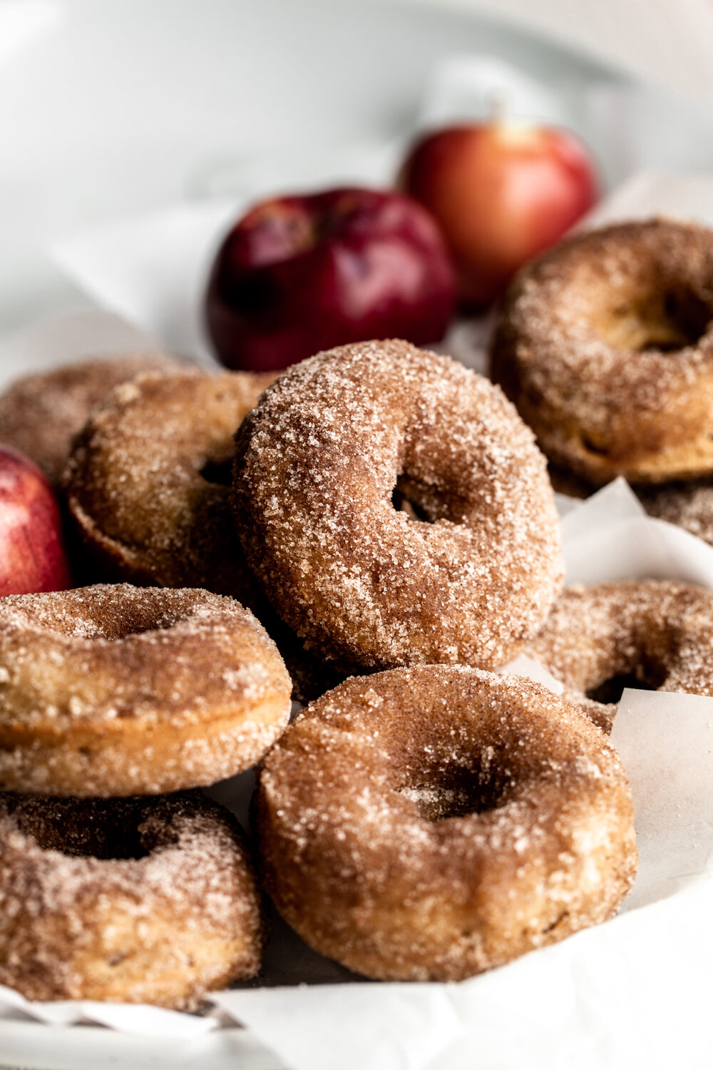 Apple Cider Donuts with red apples in the background in cinnamon sugar