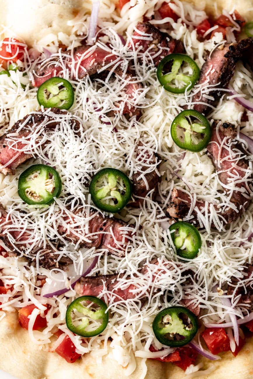 Close up of jalapeños, cheese, and steak on BBQ steak pizza.