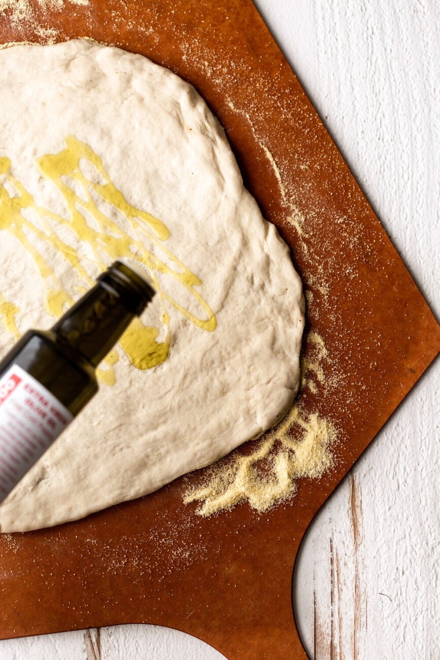 Drizzling olive oil on pizza dough, spread out on pizza peel with a dusting of corn meal around it. 