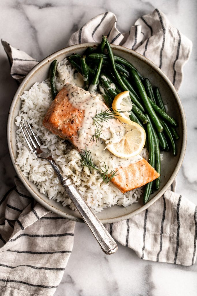 baked salmon with lemon dill cream sauce over white rice with green beans topped with lemon wedge