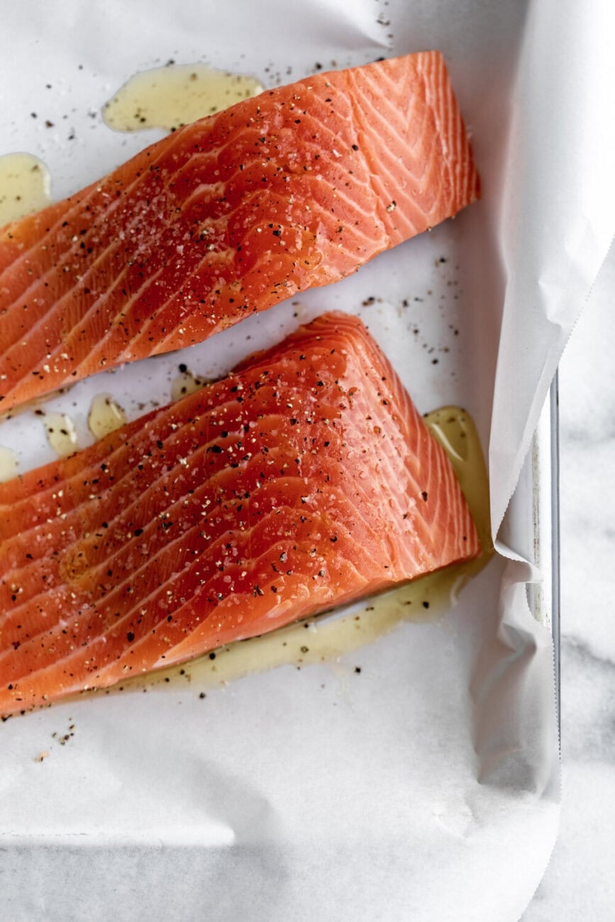 Atlantic salmon fillets topped with olive oil salt and pepper on baking sheet.