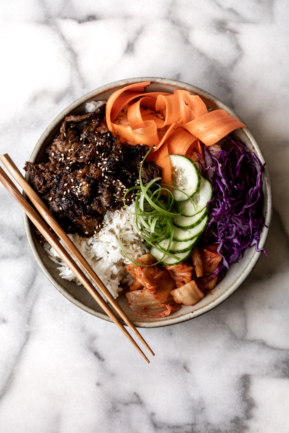 Bulgogi, Korean BBQ beef served over rice with carrots cabbage cucumber and kimchi 