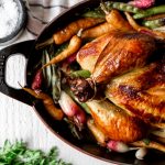 roasted chicken in a red baking dish overhead shot with peas and carrots