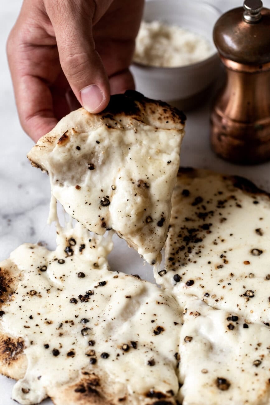 piece of cacio e pepe pizza lifted in air.