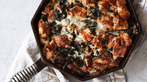 Cheesy mushroom and kale brioche strata with pancetta in cast iron pan.