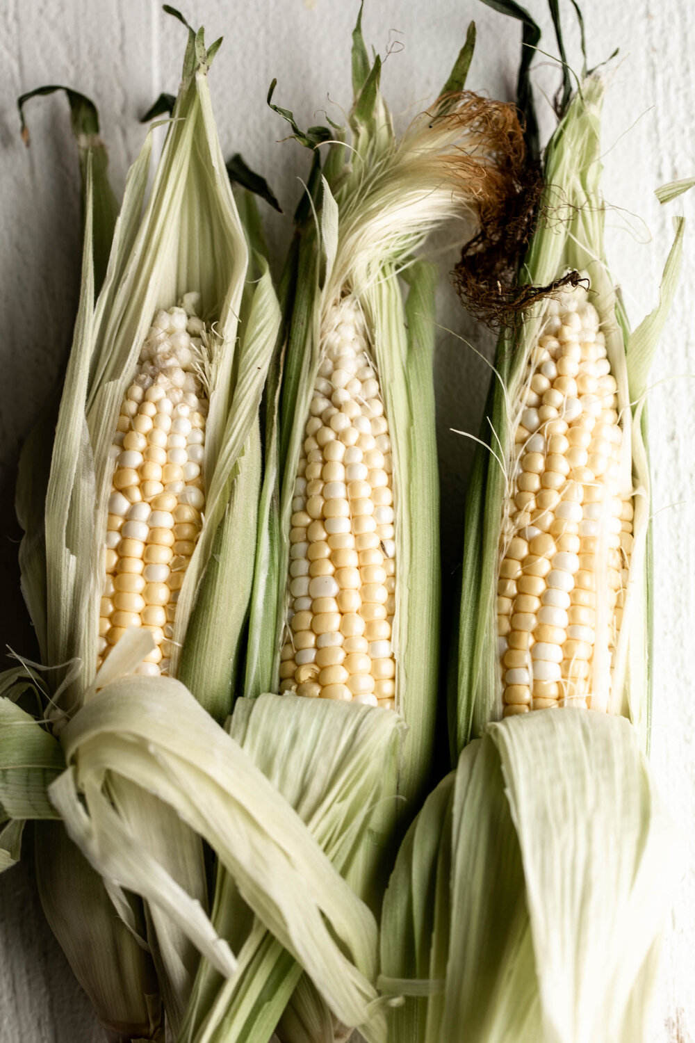 three ears of corn husks peeled back