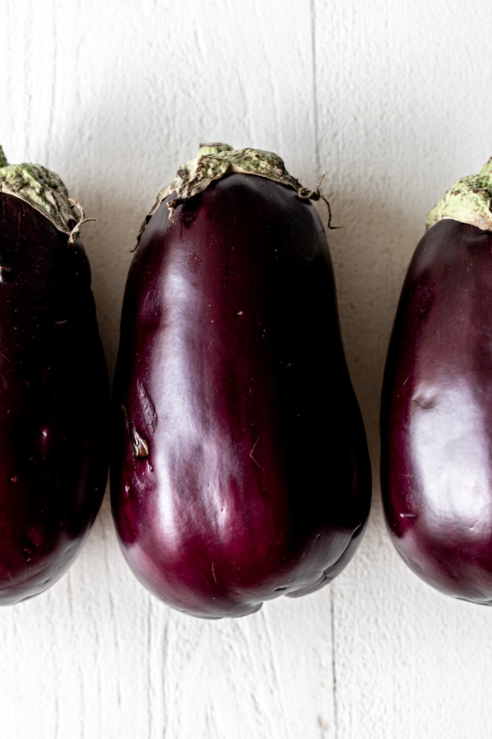 three eggplants on white wood background