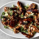 Garlic soy chicken wings topped with herbs, sliced green onion and peanuts on a platter.