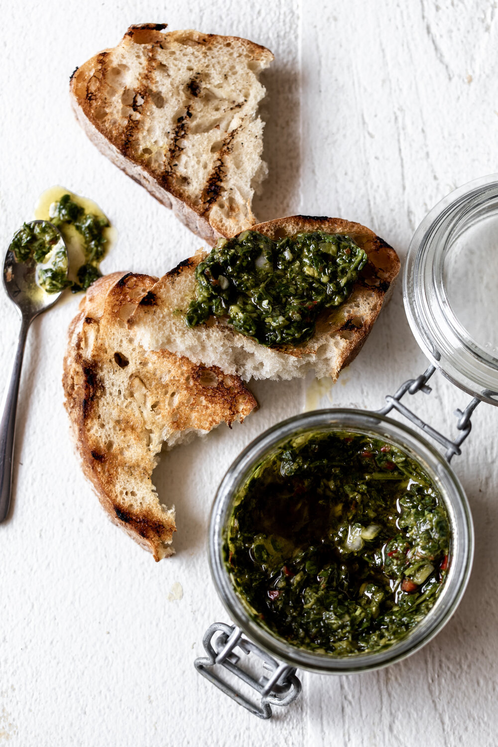 homemade chimichurri sauce in glass jar spread on grilled bread