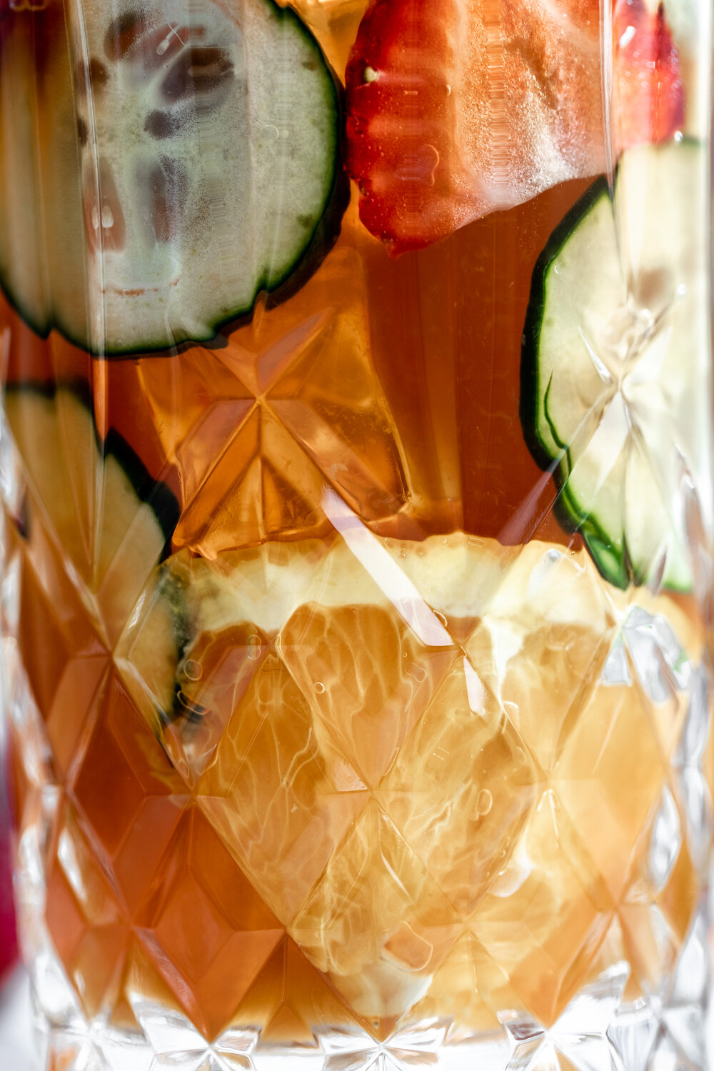 Pimm's Cup gin liqueur cocktail recipe with strawberries cucumber and orange slices in a crystal high ball glass