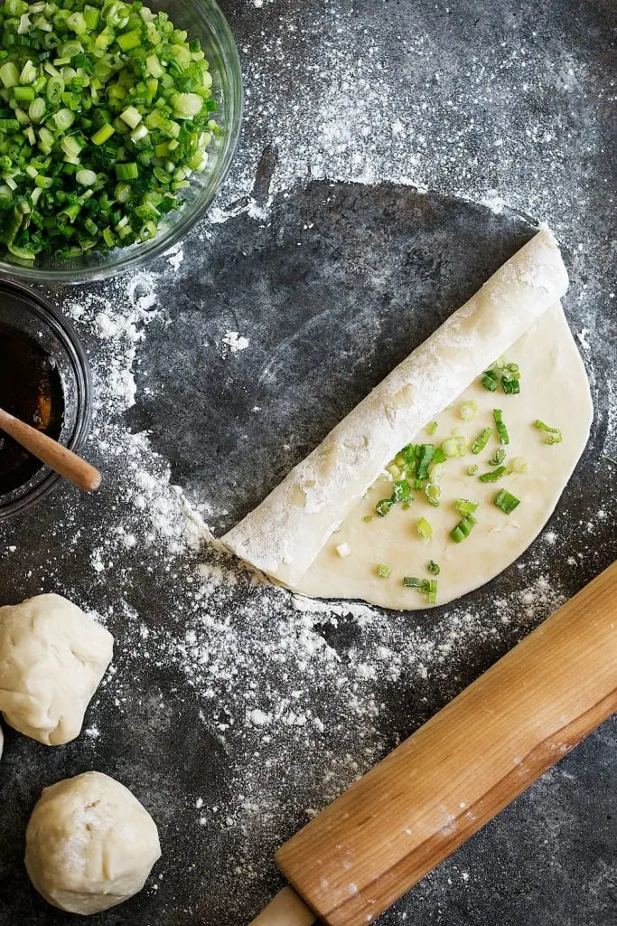 Chinese-style scallion pancake dough rolled out painted with sesame oil and topped with green onions rolled up step 3