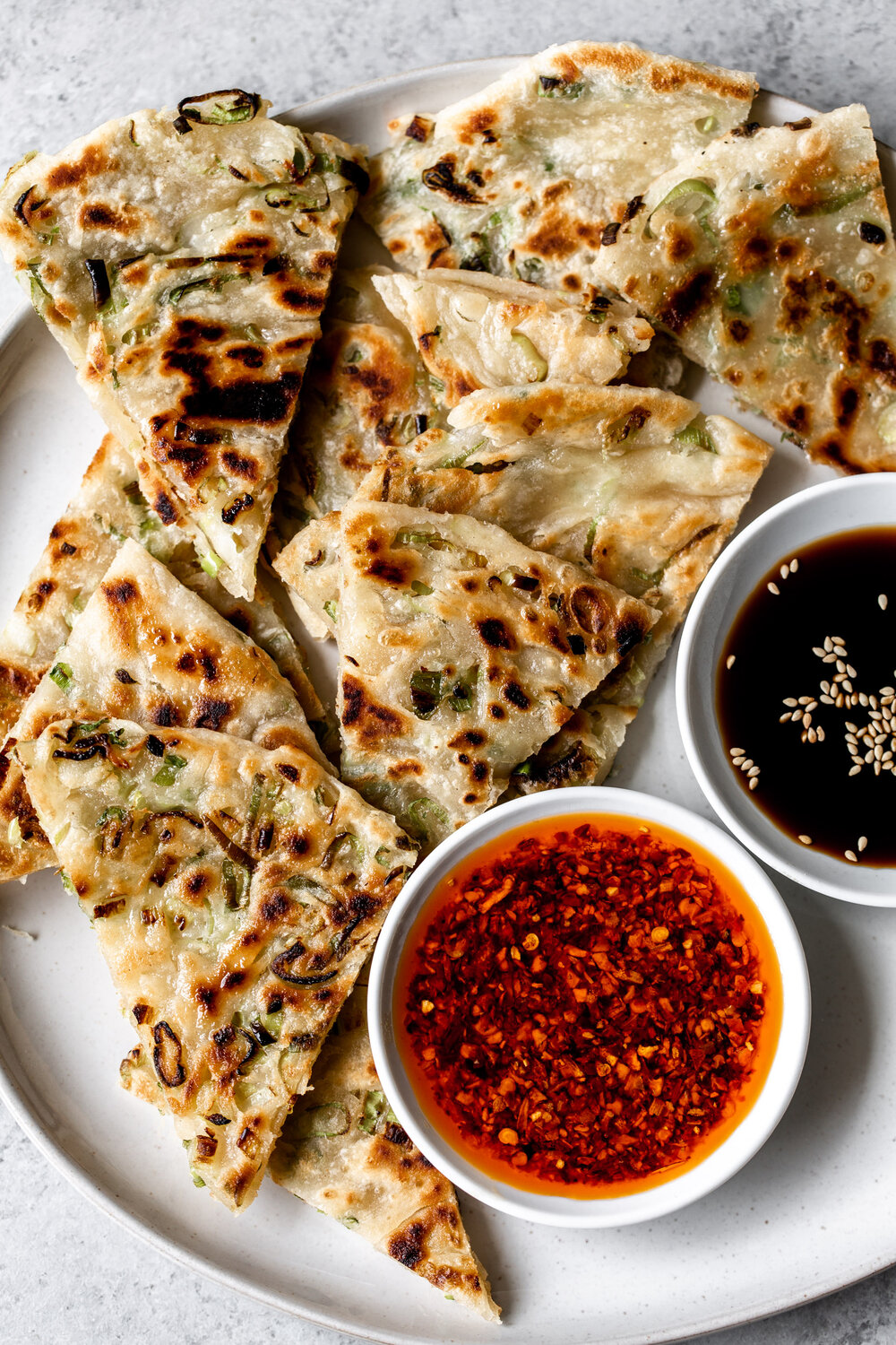 closeup of Chinese-style Scallion Pancakes cooked in a skillet served on a plate with chili crisp and Chinese black vinegar