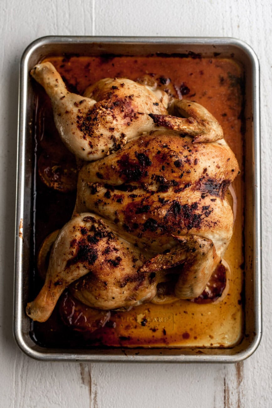 spatchcocked lemon and garlic roast chicken on baking sheet.