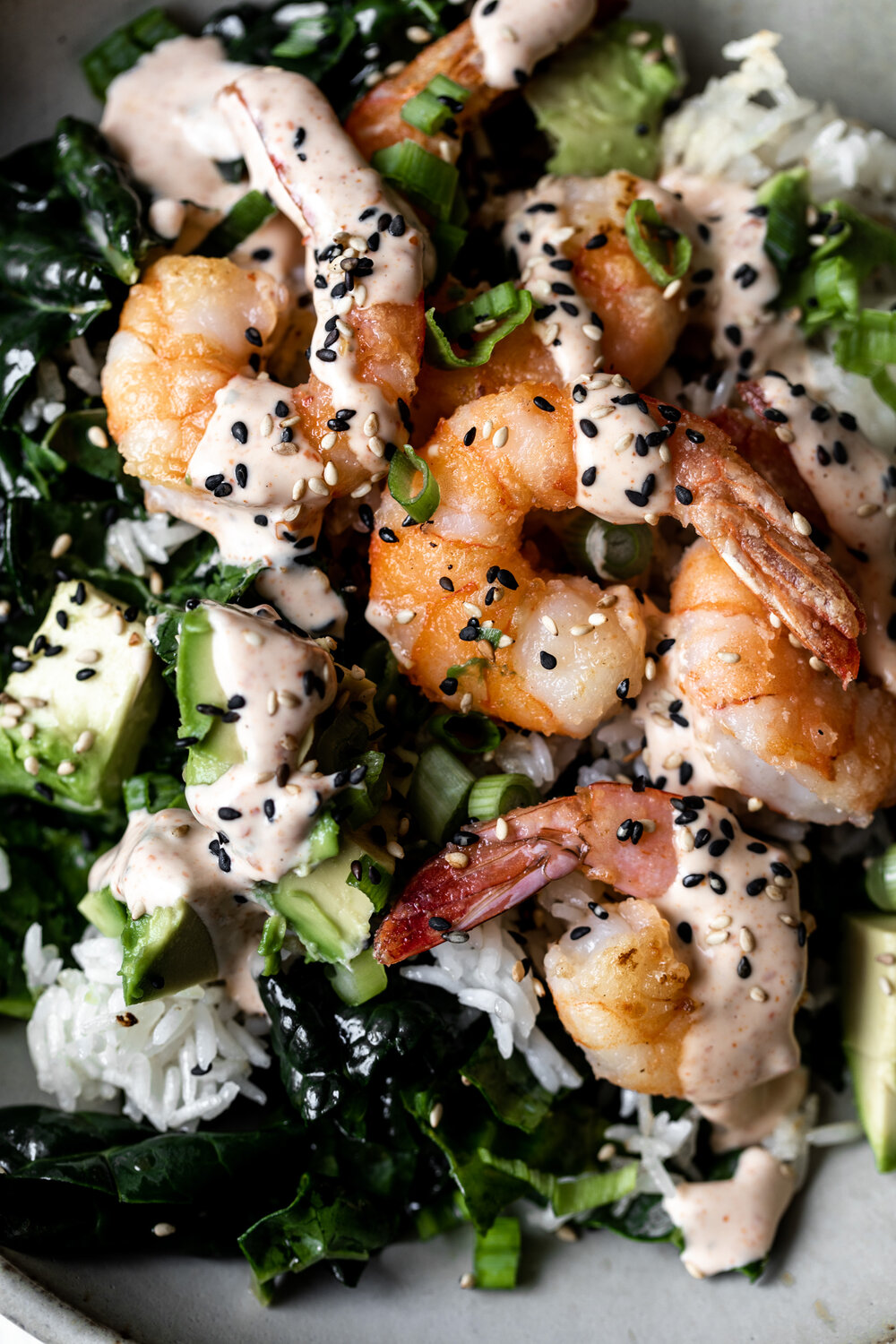 Healthy-ish shrimp bowls with crispy shrimp avocado and green onion over crispy rice and kale topped with a spicy togarashi mayo sauce.