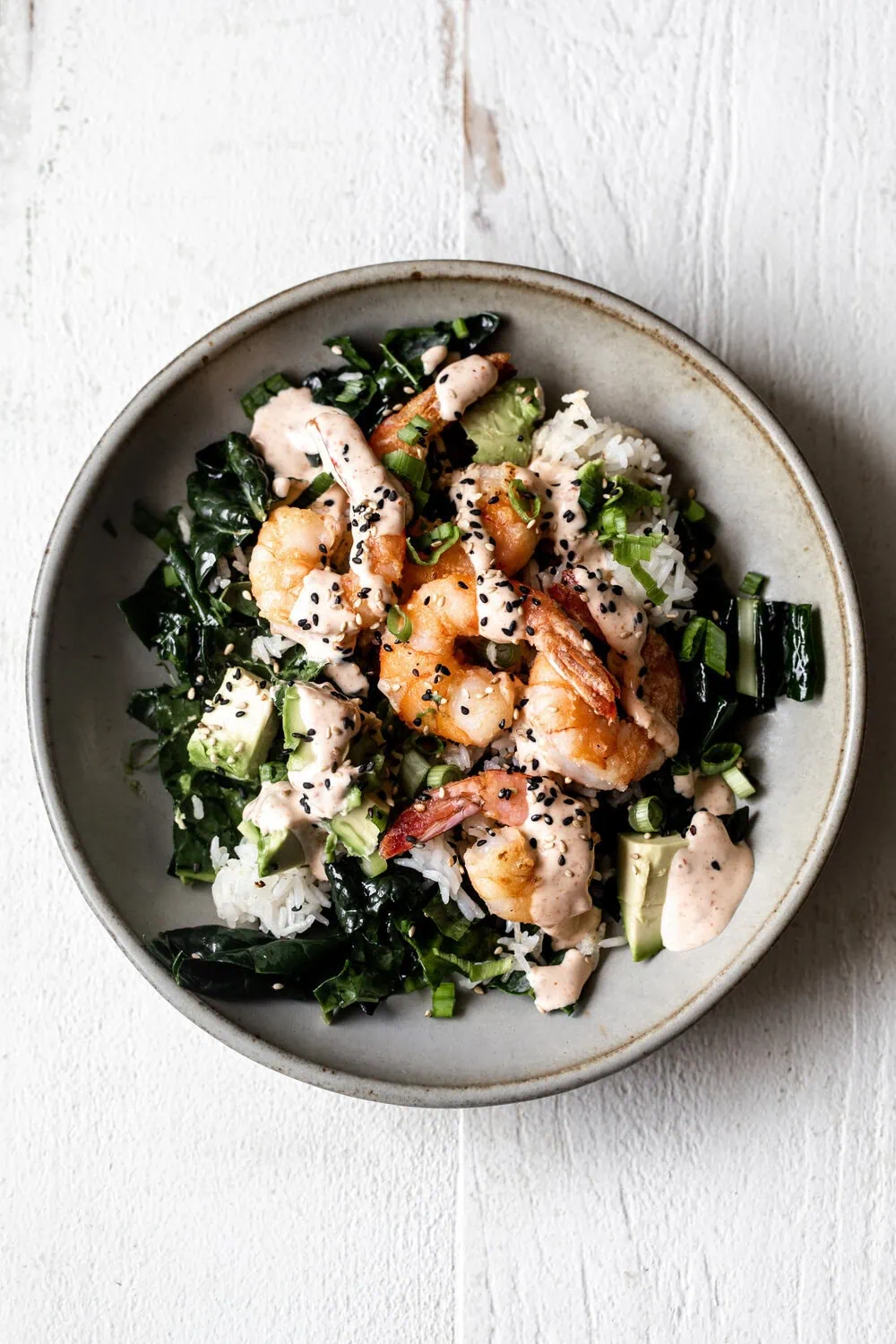 Healthy-ish shrimp bowls with crispy shrimp avocado and green onion over crispy rice and kale drizzled with spicy togarashi mayo sauce