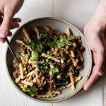 gemelli pasta noodles with lamb sausage and peas in a stoneware bowl held in hands with a fork
