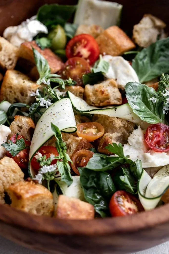 closeup Tuscan-style panzanella salad with tomatoes, zucchini, basil and mozzarella in a wood bowl