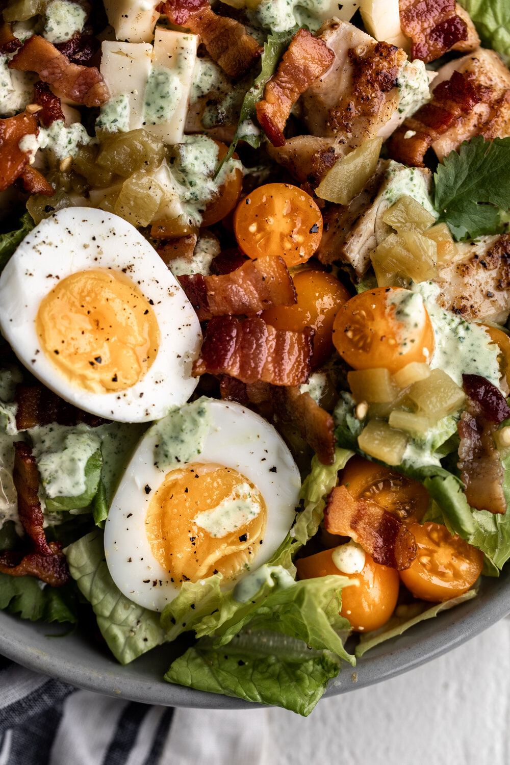 closeup of Tex-Mex Cobb salad with romaine, buttermilk cilantro ranch, chicken thighs, bacon, diced green chilies topped with soft-boiled eggs 