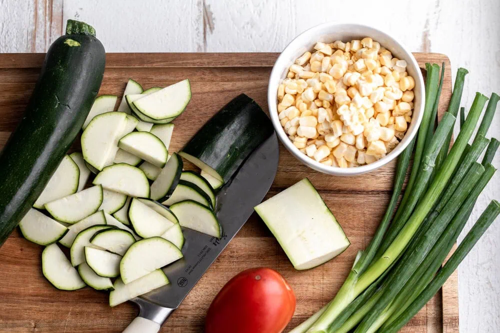 sliced zucchini tomatoes corn and green onions on cutting board