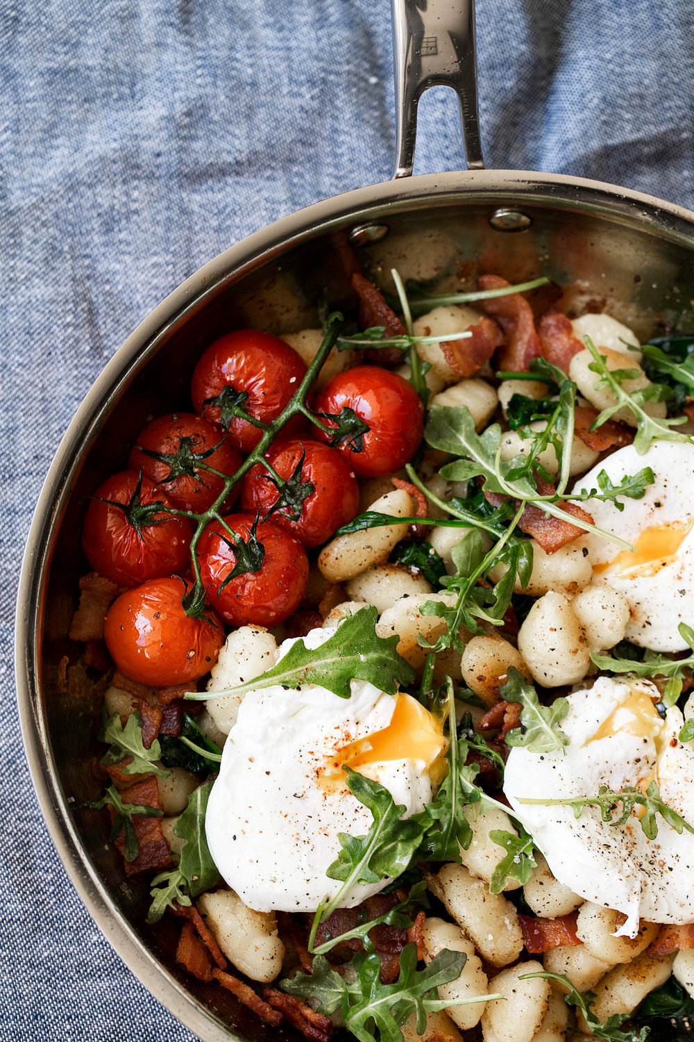 breakfast gnocchi in pan with tomatoes bacon poached eggs and arugula garnish