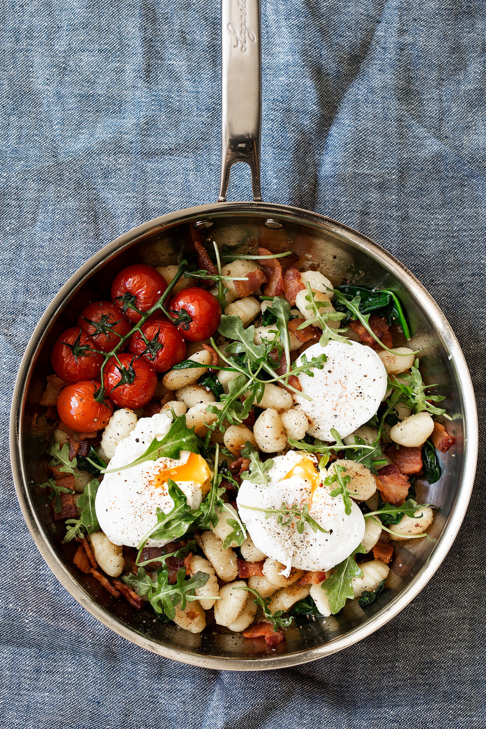 breakfast gnocchi in pan with tomatoes bacon poached eggs and arugula garnish