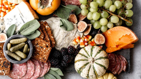 orange and yellow cheeses are served on a grey marble board for a halloween feel with green grapes, mini pumpkins and figs