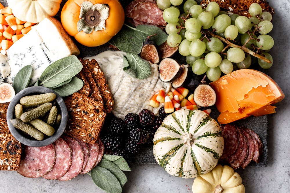 orange and yellow cheeses are served on a grey marble board for a halloween feel with green grapes, mini pumpkins and figs