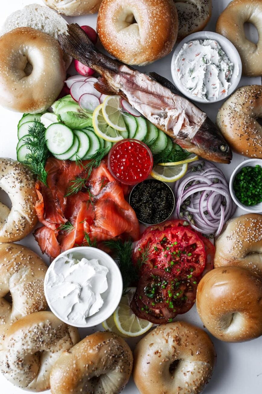 Bagel brunch ingredient shot with bagels, salmon, cream cheese, sliced onion, sliced cucumber, heirloom tomatoes, salmon roe and sturgeon caviar.