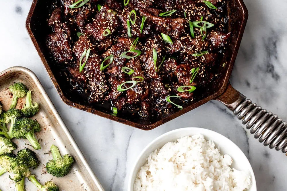 mongolian beef ingredients in cast iron pan with white rice and broccoli