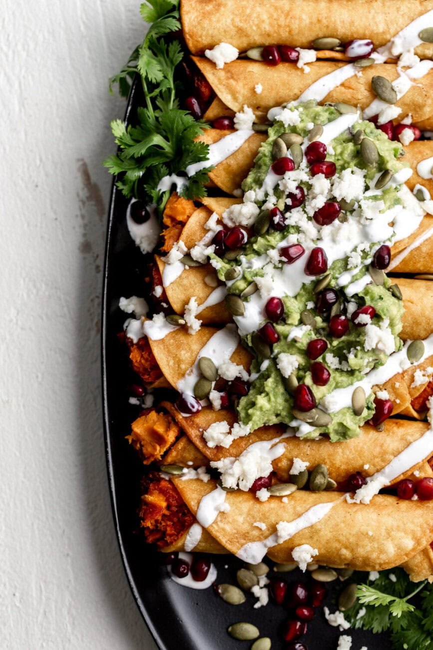 Sweet Potato Taquitos with Pomegranate & Pumpkin Seeds topped with guacamole and sour cream.