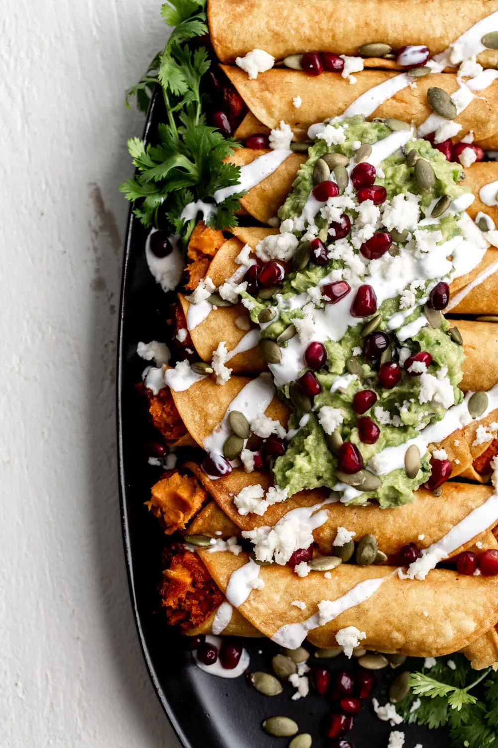Sweet Potato Taquitos with Pomegranate & Pumpkin Seeds topped with guacamole and sour cream