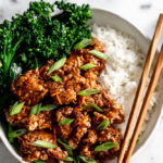 crispy orange chicken garnished with green onions paired with broccolini.