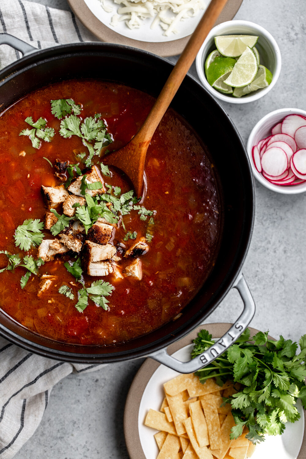 Chicken Tortilla Soup in pot with limes radish cilantro and tortilla strips