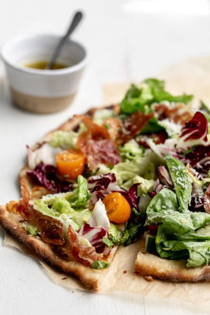 East Coast meets West Coast mashup with crispy thin crust pizza is topped with a light salad with avocado and crispy prosciutto