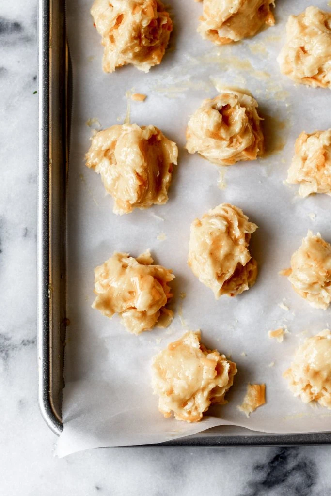 cheddar and lobster filled choux pastry dough dropped on a parchment paper lined baking sheet