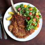 fried bone in veal milanese dish with arugula side salad and lemon.