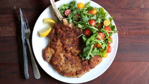 fried bone in veal milanese dish with arugula side salad and lemon.