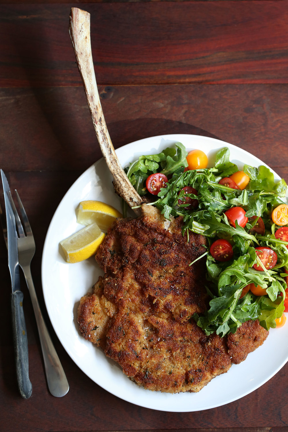 fried bone in veal milanese dish with arugula side salad and lemon