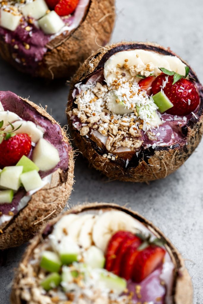 acai smoothie bowl served in opened coconuts with shredded coconut strawberries banana and green apple