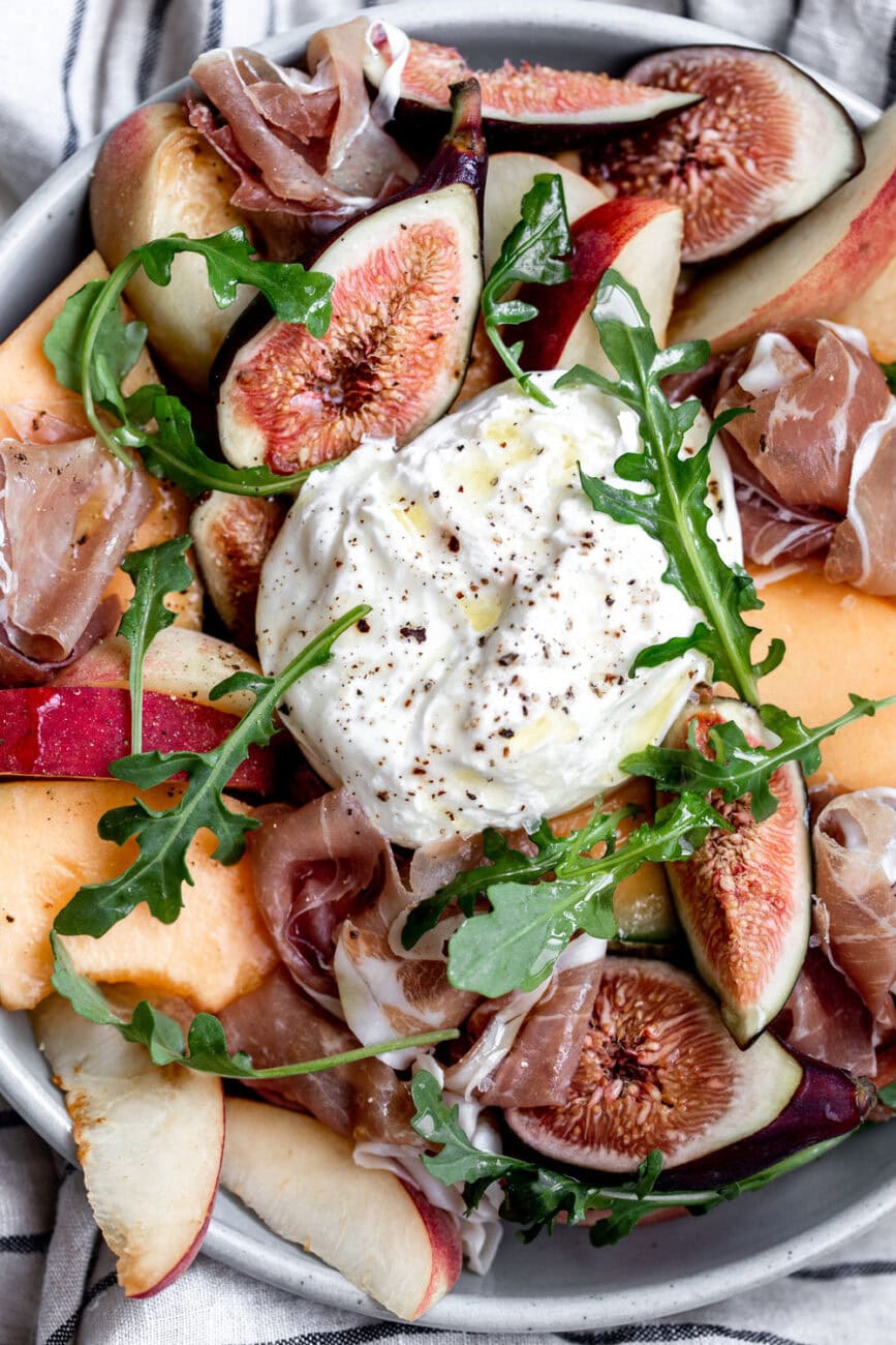 summer fruit salad with burrata and prosciutto in bowl.