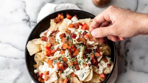 homemade potato chips topped with blue cheese fondue, diced roma tomatoes and chives in a black stone bowl on a marble table