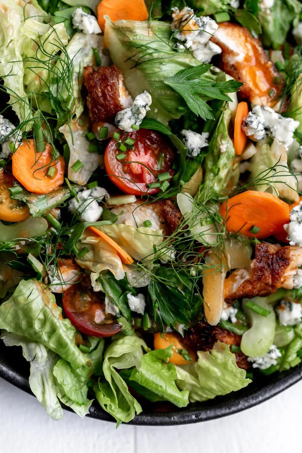  Fried Buffalo Chicken Salad recipe with halved tomato, pickled carrots and herbs.