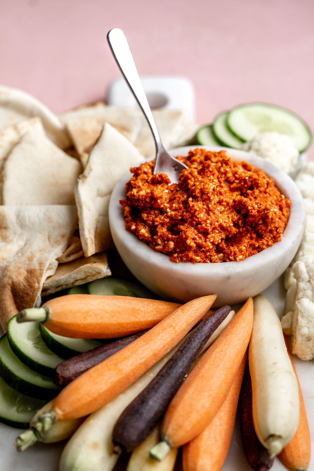 Spicy Feta Dip recipe in marble bowl with pita, cucumber and carrots on pink background